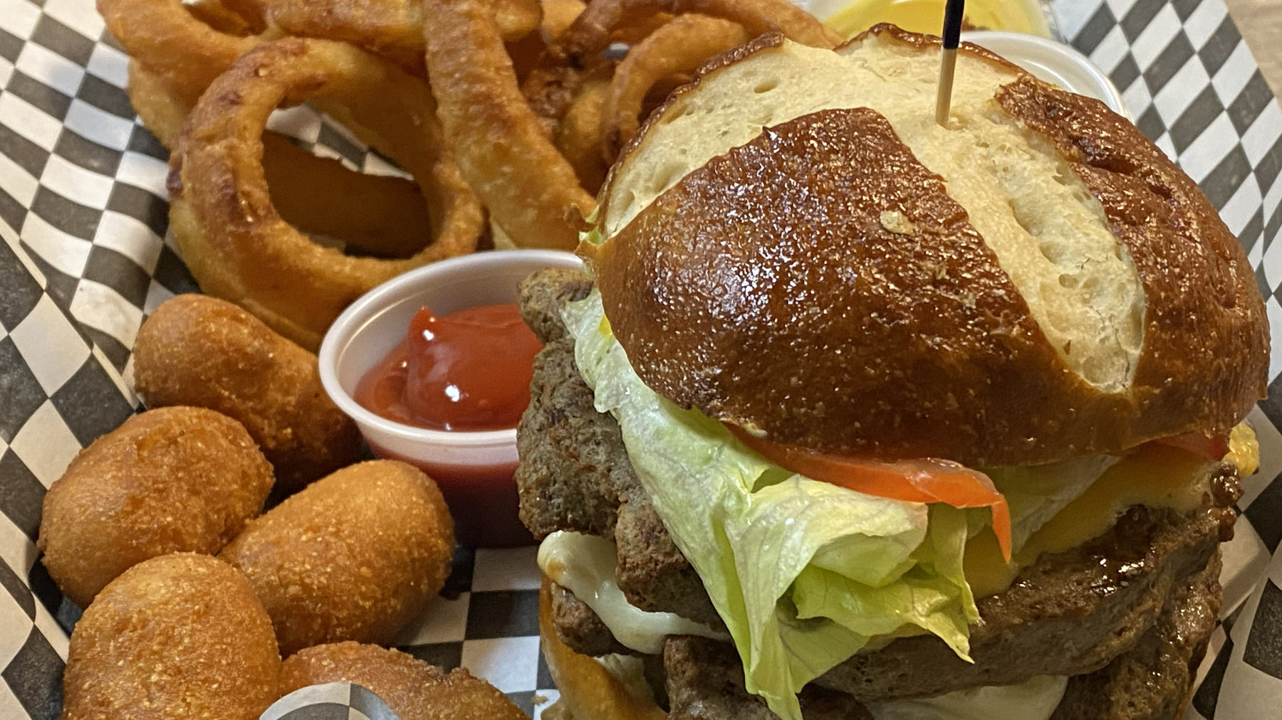 Burger with lettuce, tomato, and cheese on a bun, accompanied by onion rings and a side of ketchup.