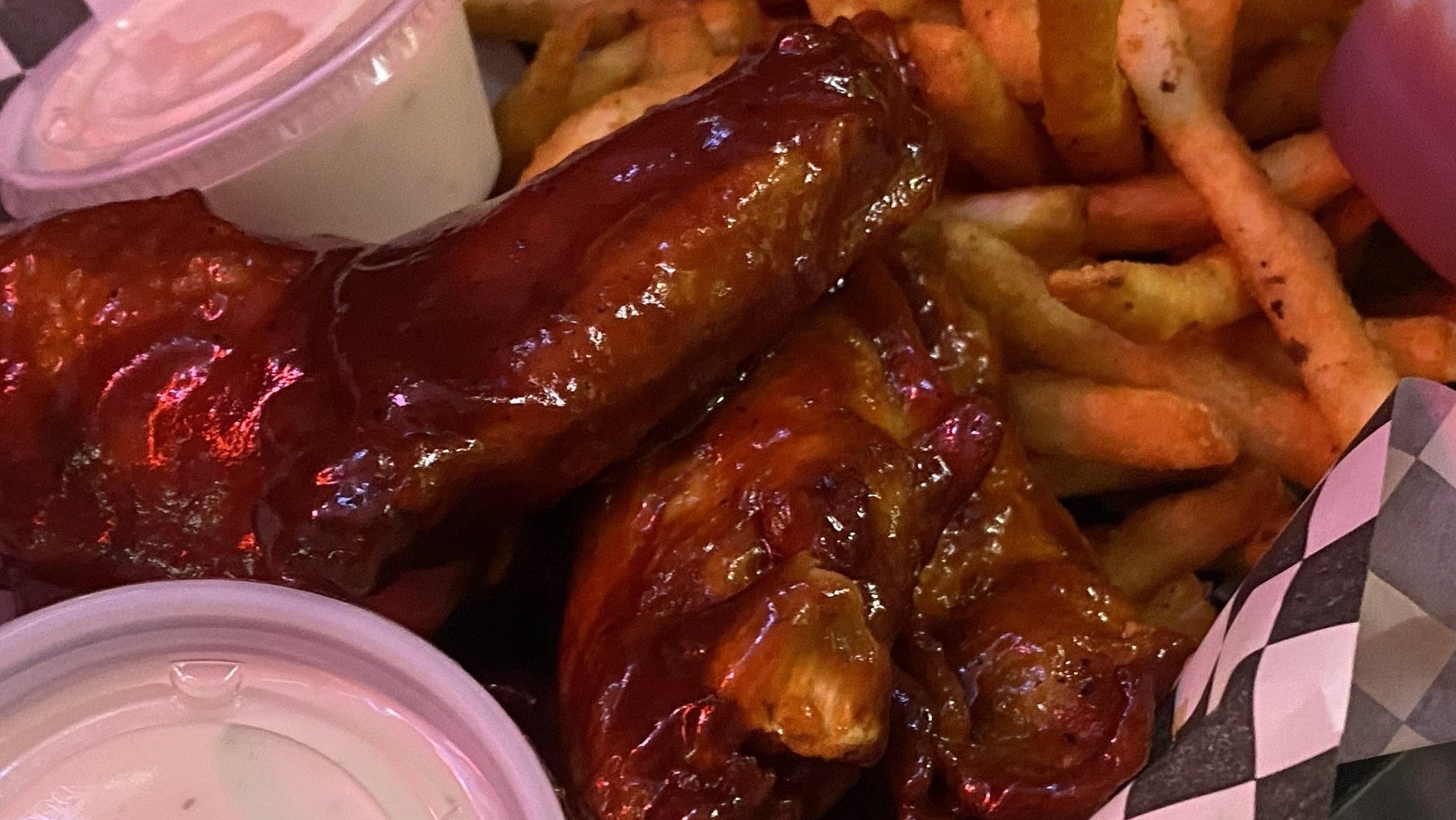 Basket of wings and fries with sauces on a checkered paper liner.